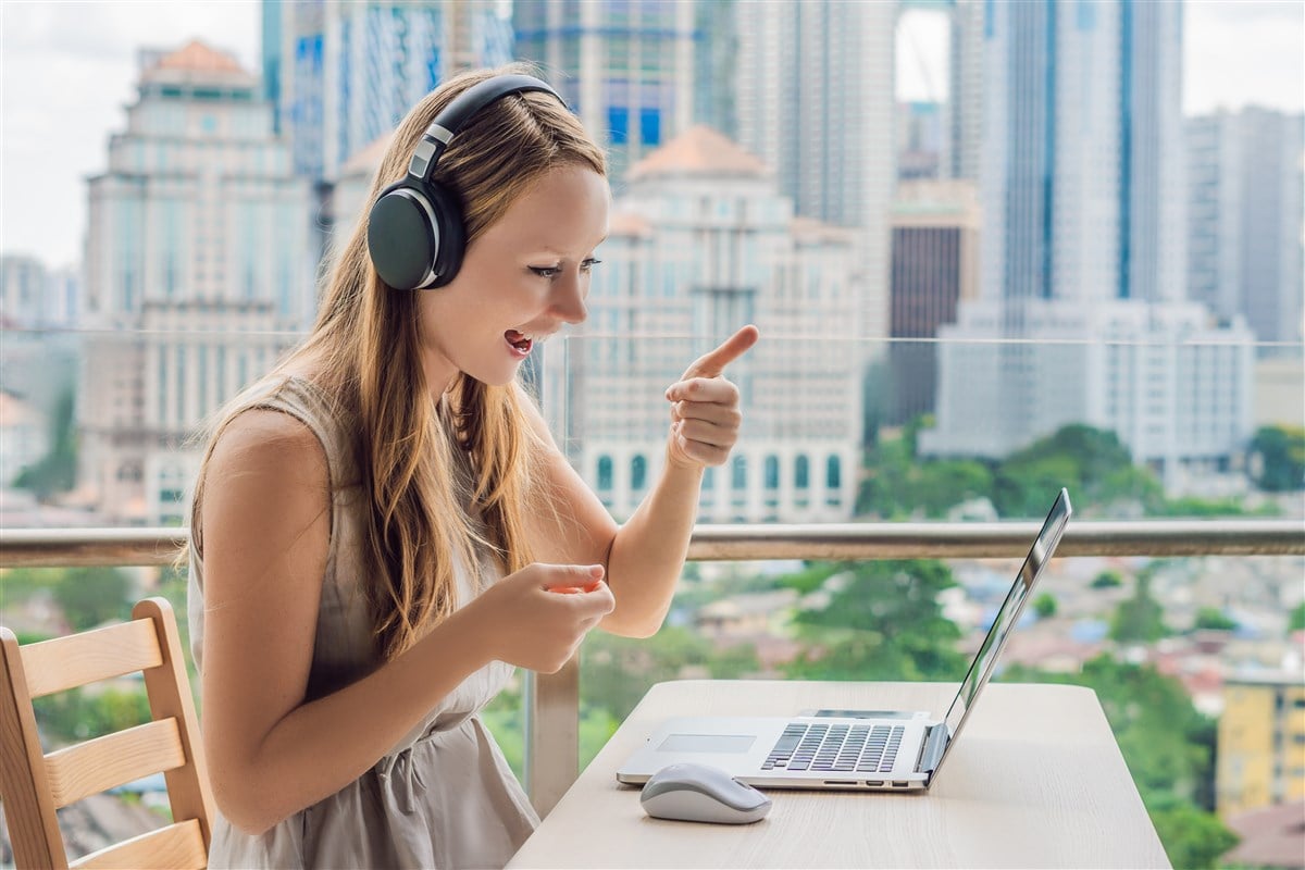 Photo of a smiling woman with headphones learning a language on laptop
