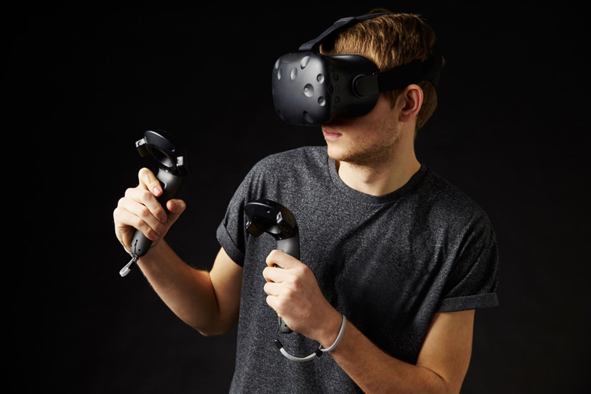 Photo of a young man wearing a virtual reality headset and using controllers. How to invest in virtual reality.