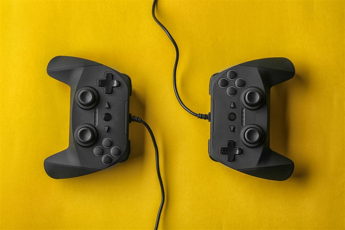 Photo of two video game controllers on bright yellow background. How to Invest in Gaming.