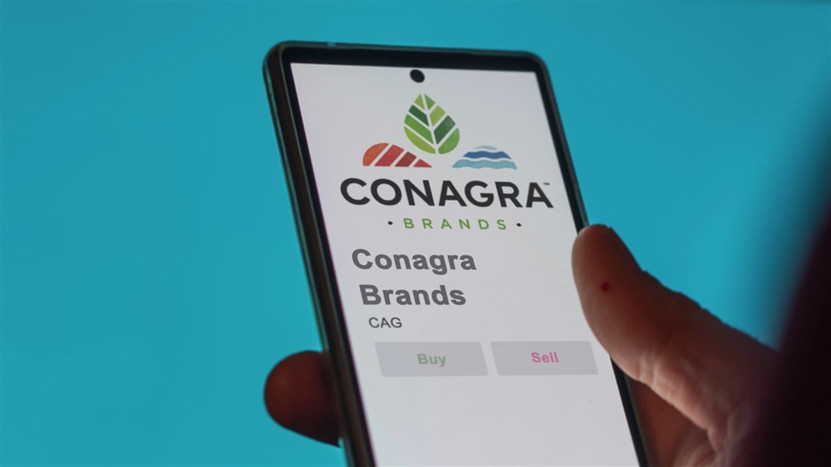 Close up on logo of Conagra Brands on the screen of an exchange. Conagra Brands price stocks, $CAG on a device.