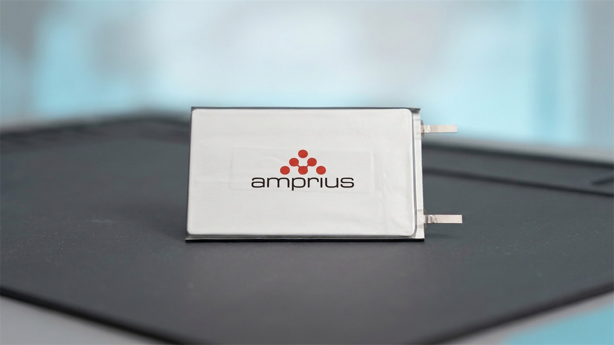 Amprius lithium battery pouch cell with the company logo on a silver casing resting on a dark surface in a lab setting.