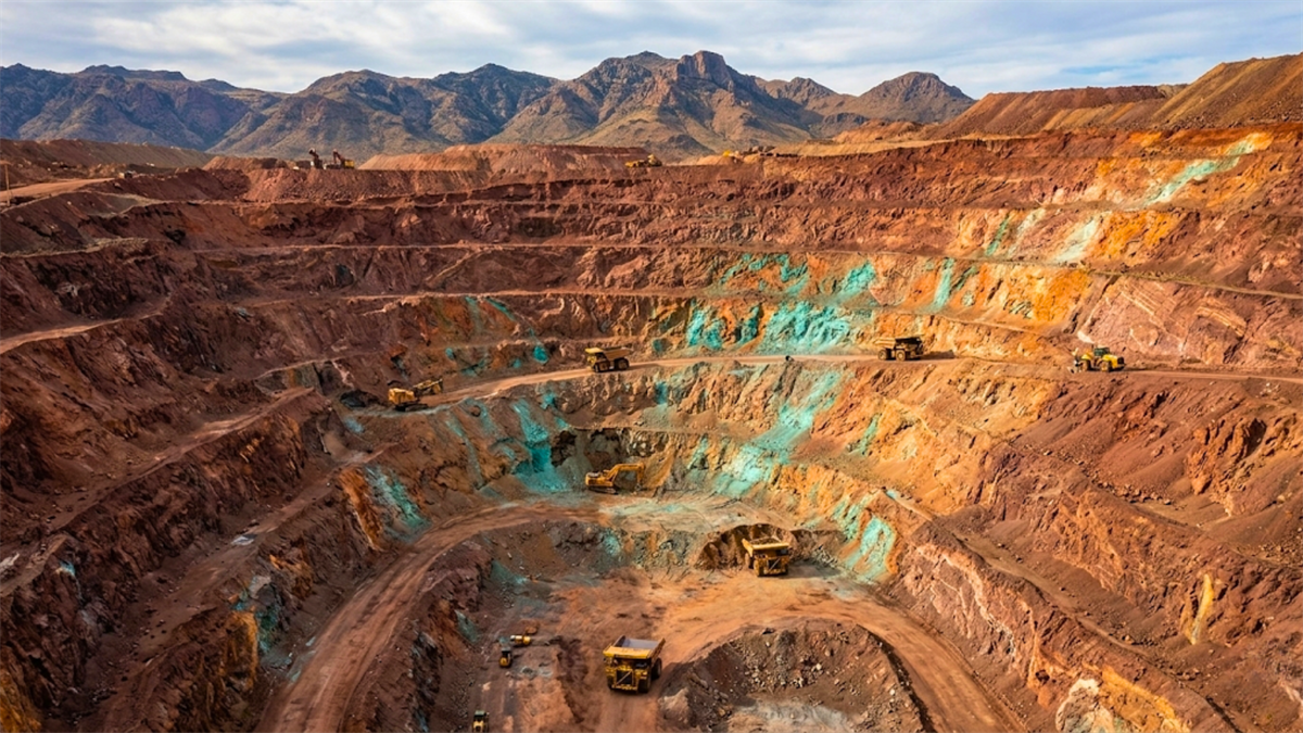 Open-pit copper mine with haul trucks on terraced benches.