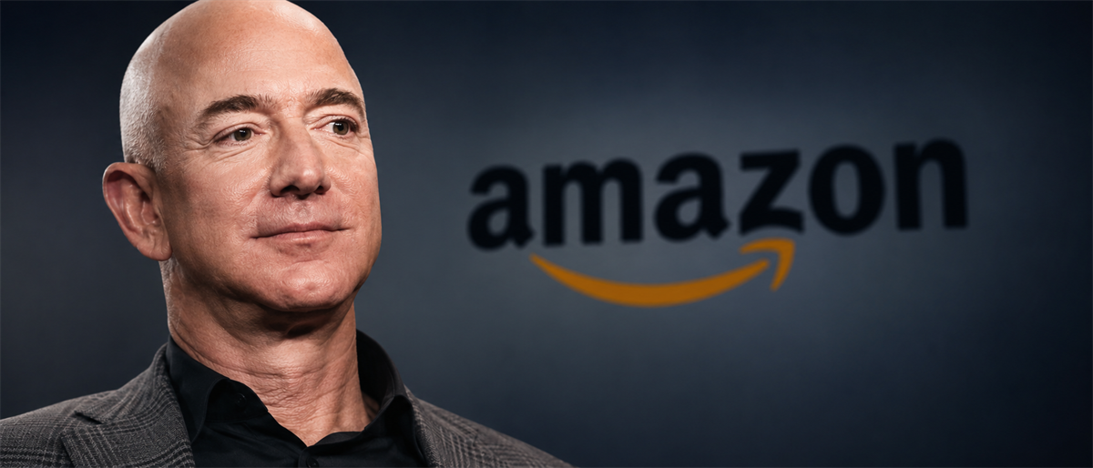 Jeff Bezos in a suit stands in front of the Amazon logo displayed on a dark background.