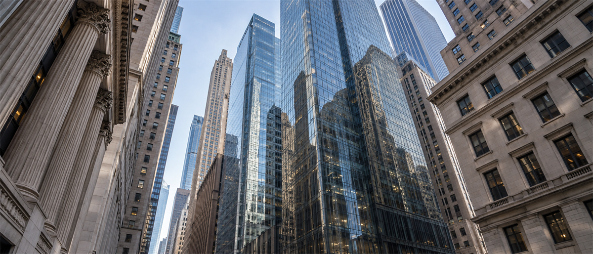Upward view of modern glass skyscrapers and classical stone buildings in a downtown financial district.
