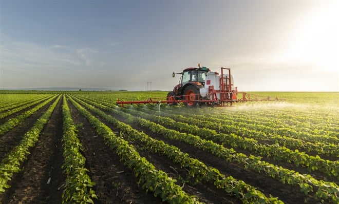 Beyond investing in physical farmland, you can invest in farmland ETFs; image of a tractor spraying a field