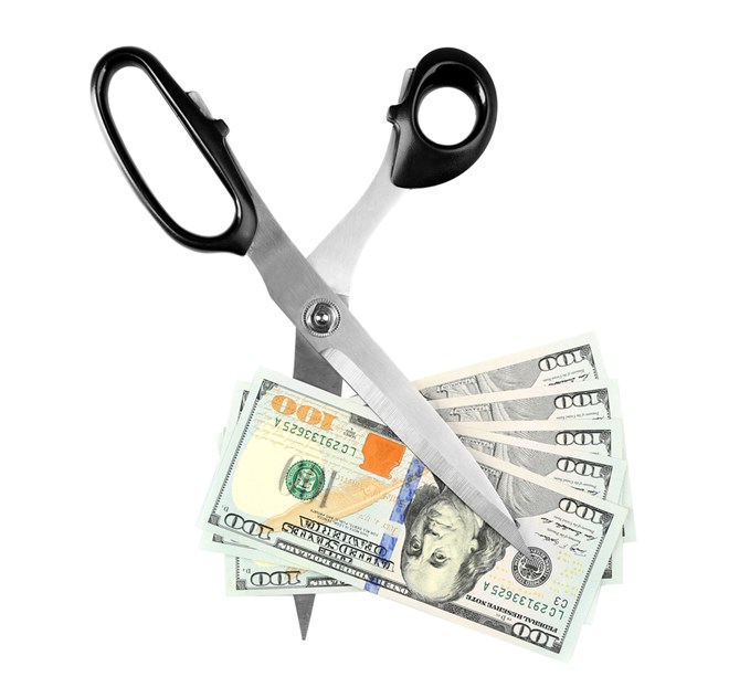 Scissors cut dollar banknotes to signify dividend cuts