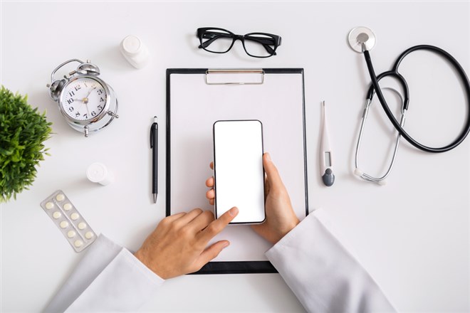 Modern technologies in healthcare sector. Male doctor using smartphone with blank screen at workplace, top view