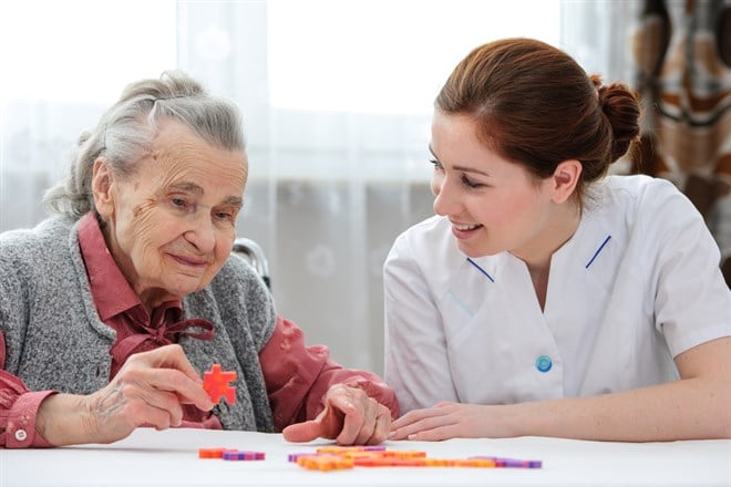 Elder care nurse playing jigsaw puzzle with senior woman in nursing home; these leaders are developing neurodegenertive disease solutions