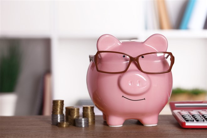 Piggy bank in glasses with calculator and coins on home or office background; How to invest in an IRA in six simple steps