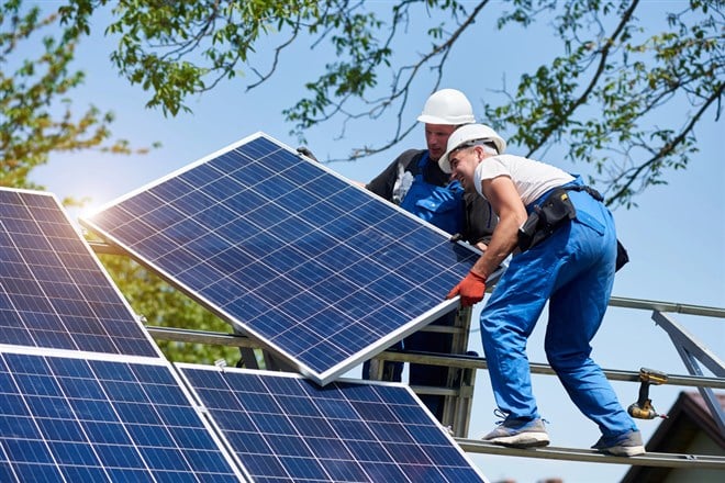 Photo of two men installing a solar panel on a roof. Nextracker: Solar Stock Soars with New Highs on the Horizon.