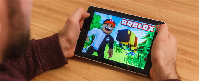 Photo of a man holding a tablet with Roblox game on it