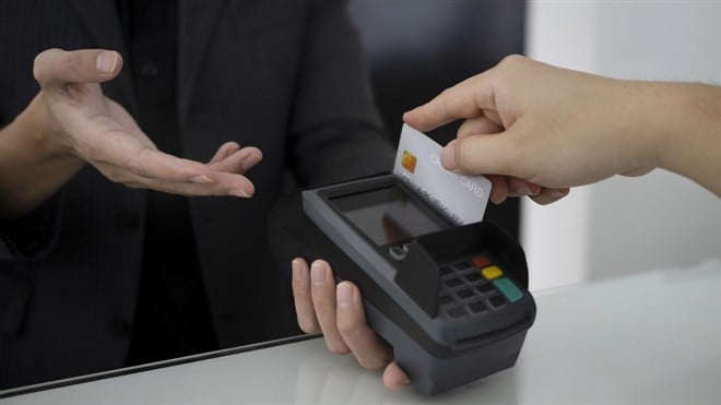 Close up of man swiping credit card through terminal for payment in restaurant.