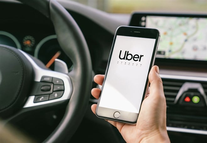 Uber driver holding smartphone in car. Uber is an American compa