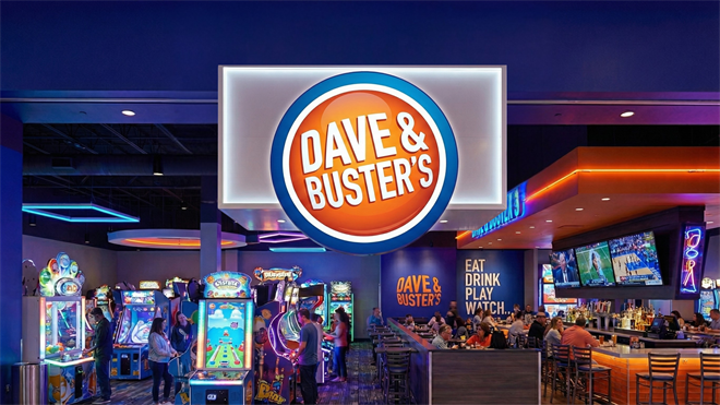 Interior of a Dave & Buster’s with arcade games, dining area, and the large illuminated logo overhead.