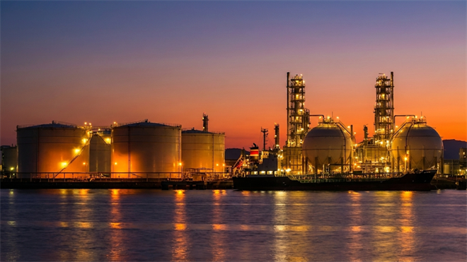 Oil and gas storage tanks glow at sunset highlighting energy infrastructure tied to fuel supply and commodity markets.