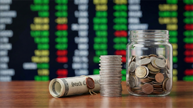 Stock certificates and coins displayed in front of stock exchange data, symbolizing income investments.