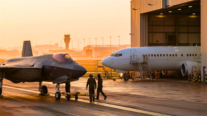Fighter jet and passenger plane in hangar at sunrise, spotlighting defense and aerospace stocks.