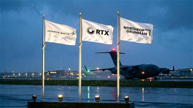 Lockheed Martin, RTX, and Northrop Grumman flags on military airfield with cargo aircraft.