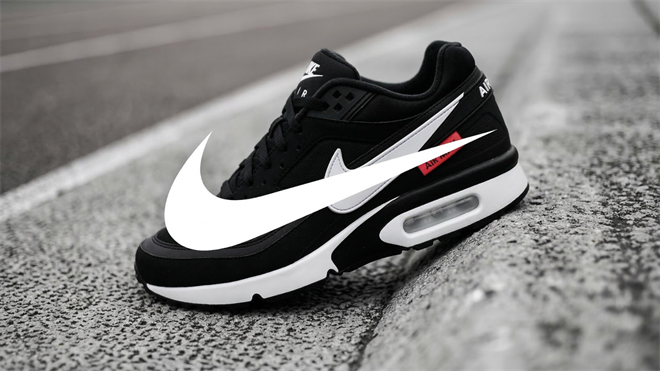 Black Nike Air sneaker with a large white swoosh resting on asphalt pavement, representing Nike’s athletic footwear brand.