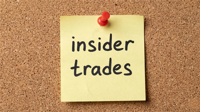 A yellow sticky note pinned to a corkboard reads “insider trades,” symbolizing insider selling activity in financial markets.