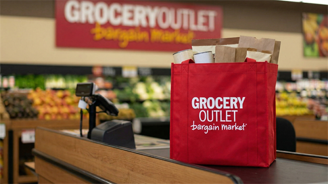 Red Grocery Outlet bag at checkout counter inside discount grocery store, reflecting value retail and insider confidence theme.
