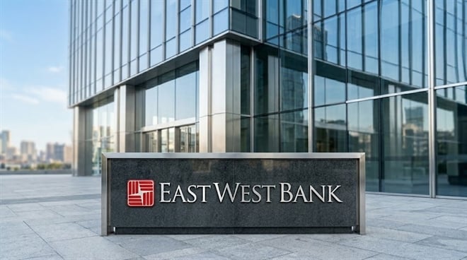 An exterior shot of a modern glass office building with a monument sign in the foreground displaying the red East West Bank logo and name.
