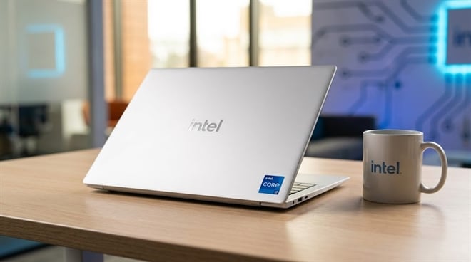 A silver laptop and a white mug, both displaying the Intel logo, sitting on a wooden desk.