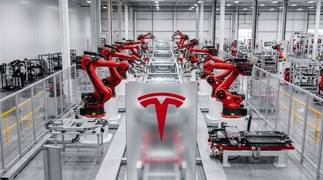 Tesla factory assembly line with robotic arms and logo.