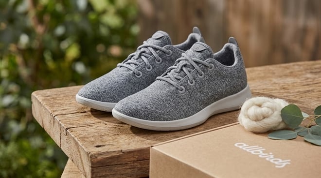 A pair of gray Allbirds wool sneakers displayed on a wooden surface beside the branded shoe box.