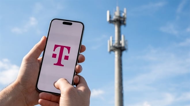 A hand holds a smartphone displaying the T-Mobile logo in front of a cell tower.