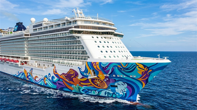 A Norwegian Cruise Line ship with colorful hull artwork sails on open ocean under blue skies.