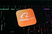 Closeup of mobile phone screen with logo lettering of alibaba.com on computer keyboard