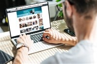 Back view of man using laptop with amazon website on screen - Stock Editorial Photography