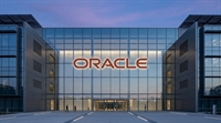 The red Oracle logo illuminated on the glass facade of a modern corporate office building at dusk.