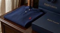 A folded navy blue Ralph Lauren polo shirt next to a branded box and shopping bag on a wooden table.