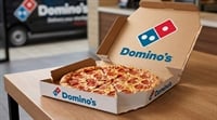 An open Domino's Pizza box containing a pepperoni pizza sits on a wooden table.