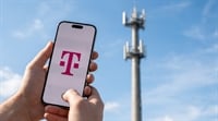 A hand holds a smartphone displaying the T-Mobile logo in front of a cell tower.