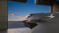 A Lockheed Martin F-35 fighter jet sits inside a hangar at dusk, bearing the company logo.