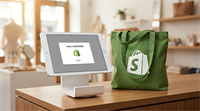 A Shopify-branded tablet point-of-sale display and green tote bag sit on a retail counter.