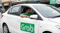 A Grab driver sits in a white sedan bearing the Grab logo on a city street.