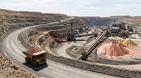 An aerial view of a large open-pit mine with a haul truck, conveyor belts, and ore stockpiles.