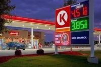 A Circle K gas station and convenience store displays fuel prices on an illuminated roadside sign at dusk.