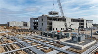 A large data center under construction with a crane, electrical transformers, generators, and conduit infrastructure visible.