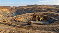 Aerial view of a large open-pit mine with haul trucks and excavation equipment on terraced roads.