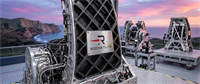 Rocket Lab-branded aerospace hardware on an outdoor platform with a coastal backdrop at sunset.