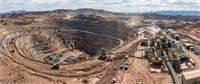 Aerial view of an open-pit mine with terraced rock walls, mining equipment, and an adjacent processing plant.