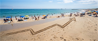 An upward-trending arrow drawn in beach sand, symbolizing rising stock prices, with beachgoers in the background.