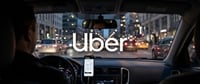 Uber logo displayed on a car windshield at night, with a driver navigating city traffic using a phone mount.