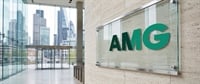 AMG logo displayed on a glass sign in an office building lobby with a city skyline visible outside.