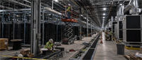 Construction workers in safety vests build server racks and infrastructure inside a large data center facility.